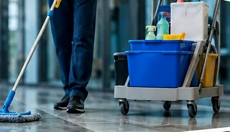 Carrinho de limpeza com baldes azuis e mop passando no piso do saguão