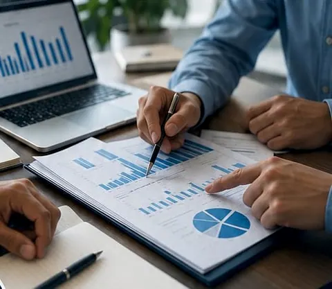 Mãos apontando os gráficos do relatório impresso, com o notebook aberto ao lado